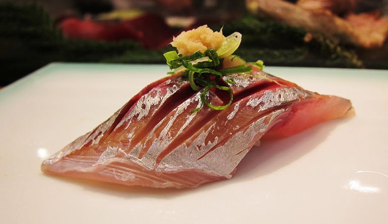 Aji Sushi auf einem Teller angerichtet, mit fein geschnittener grüner Zwiebel und geriebenem Ingwer garniert.