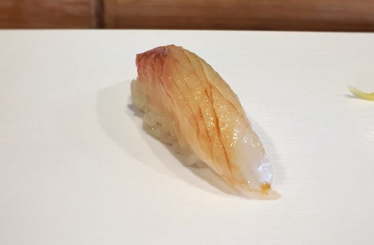 Ein einzelnes Nigiri Sushi mit glänzendem, zartem Fischbelag auf einem Teller