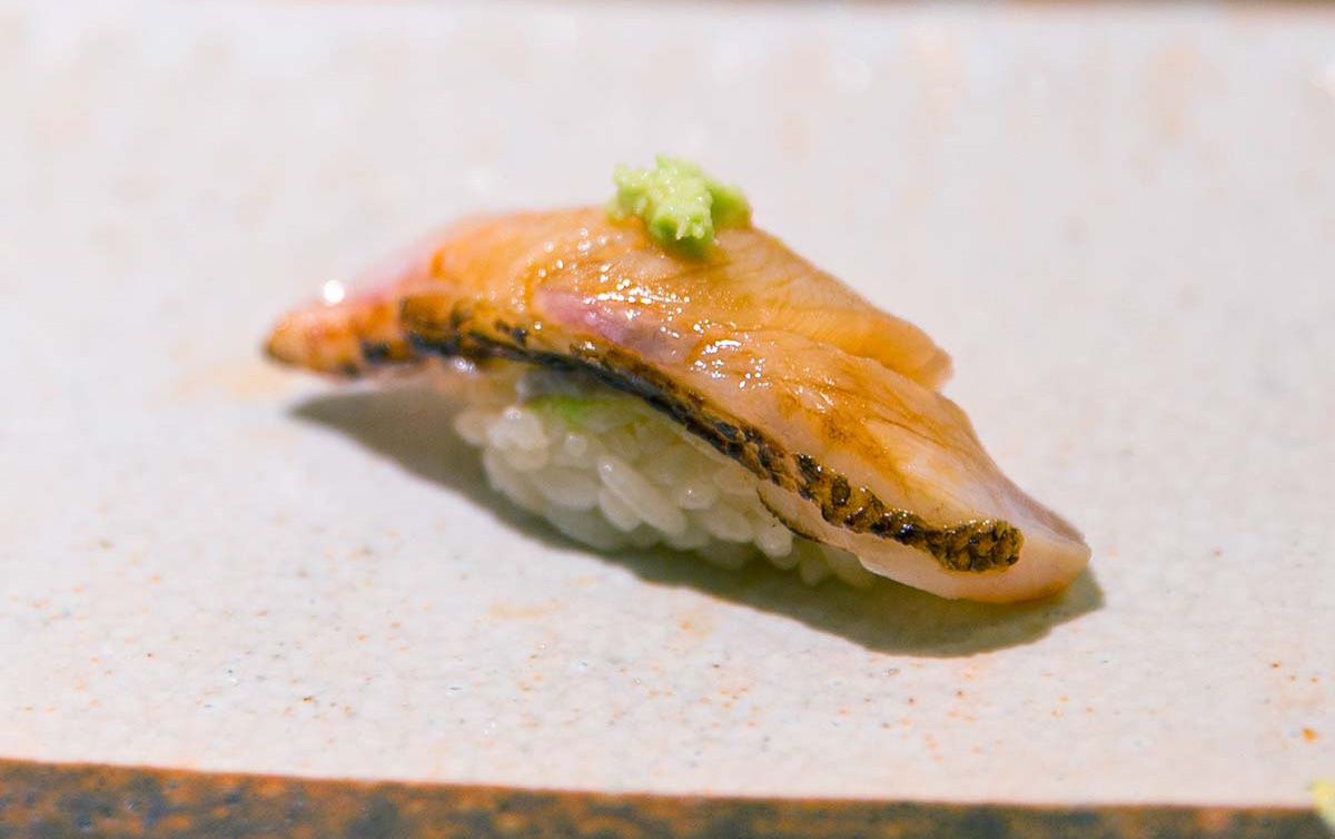 Nodoguro nigiri sushi, enhanced with wasabi, presented on a ceramic plate under clear, natural lighting