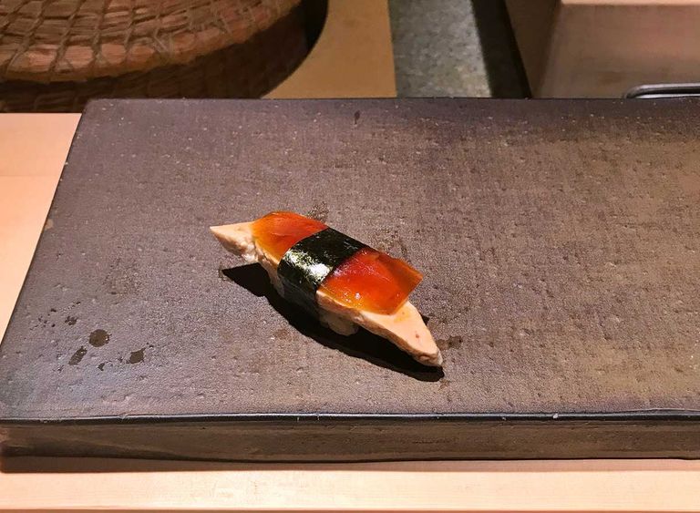 A piece of nigiri sushi with fish liver, topped with pickled watermelon, showcased on a stone slab plate