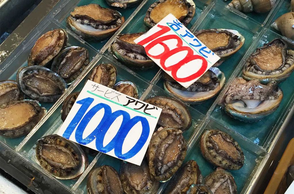 Verschiedene Größen von Awabi-Abalone auf einem japanischen Markt mit Preisschildern in Yen.