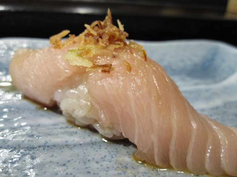 Nigiri-Sushi mit Albacore-Bauchfleisch, garniert mit frittierten Zwiebeln, auf einer blauen Keramikplatte.