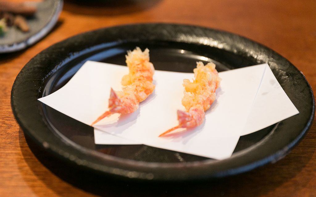 Zwei Stücke Garnelen-Tempura angerichtet auf weißem Papier, das auf einem schwarzen Teller liegt, im Mikawa Zezankyo, einem mit einem Michelin-Stern ausgezeichneten Tempura-Restaurant.