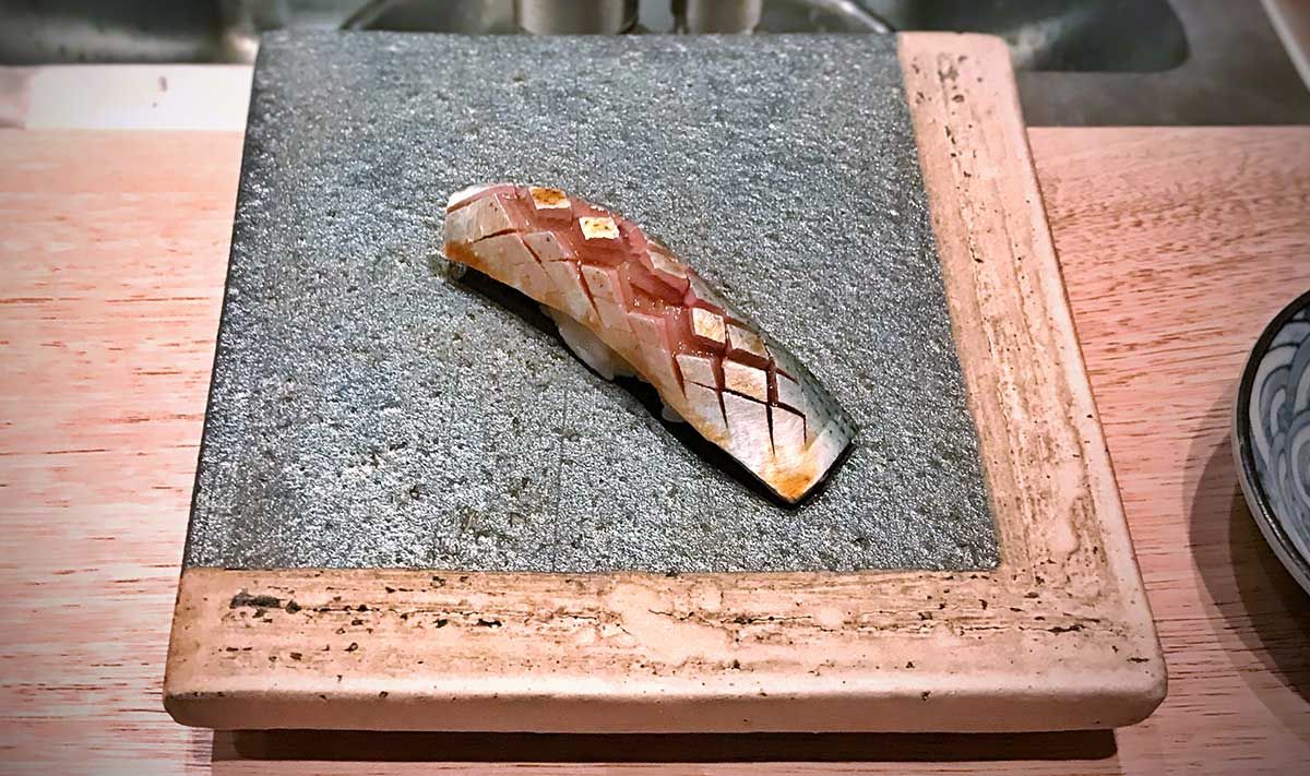 Iwashi Sushi, eine Sardinen-Nigiri, kunstvoll auf einer steinernen Platte serviert.