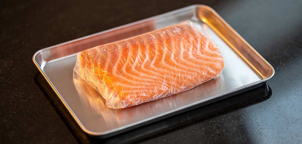 Ein Stück frisches Lachsfleisch, das auf einem Metalltablett liegt und mit Kontakt-Entwässerungsfolie umwickelt ist. Diese Folie entfernt Feuchtigkeit, um die Frische des Lachses zu bewahren, was ihn ideal für die Zubereitung von hochwertigem Sushi macht.