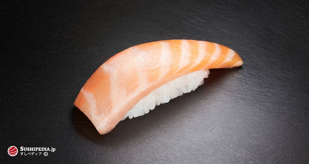 Ein Stück Lachsbauch Sushi Nigiri, platziert auf einem dunklen Hintergrund. Deutlich zu sehen ist die ausgeprägte Maserung des Bauchfetts.