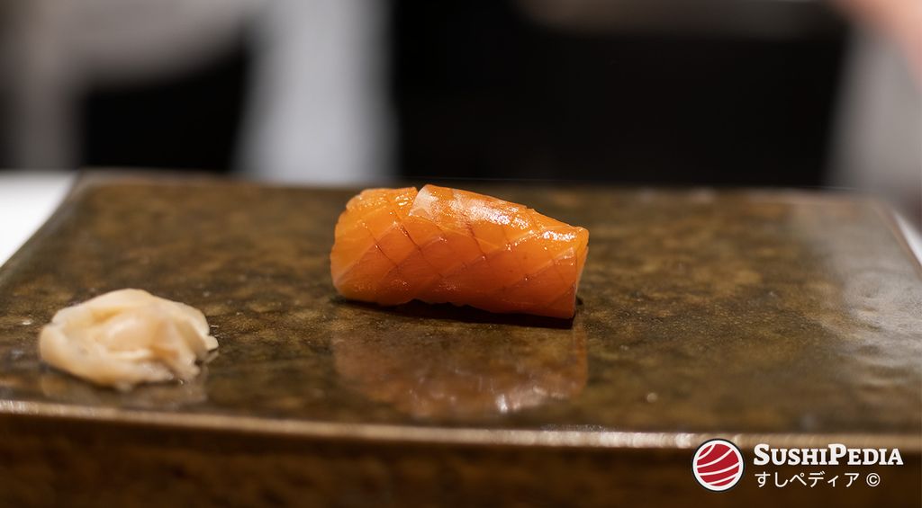 Ein Stück Lachs-Sushi (Samon oder Sake-Sushi), garniert mit Konbu, liegt auf einer traditionellen Keramikplatte.