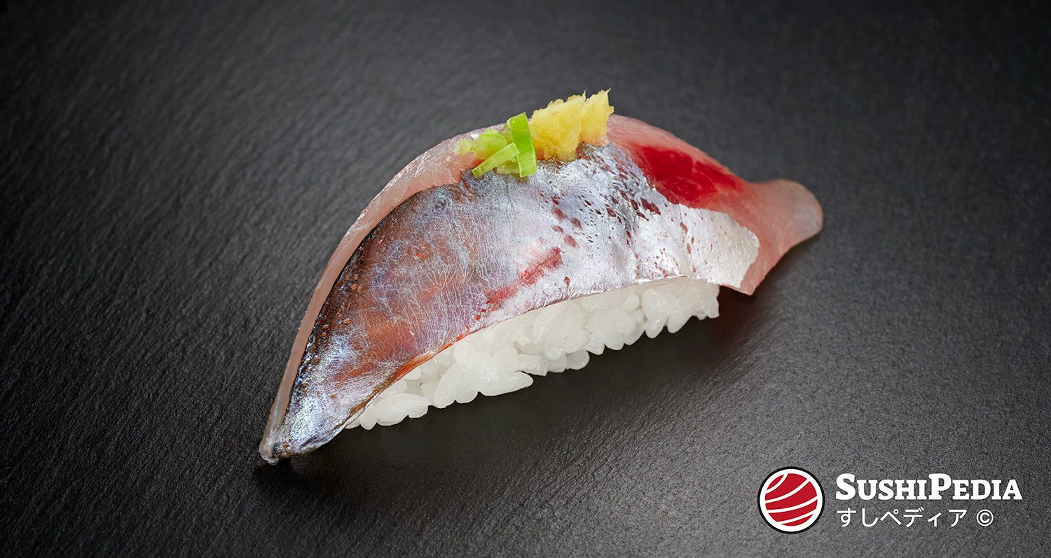 Ein frisch zu bereitetes Stück Sushi, mit der Zutat Aji, liegt auf einer Schieferplatte. Der Name Aji steht im Japanischen für die Bastardmakrele bzw. die Familie der Stachelmakrelen.