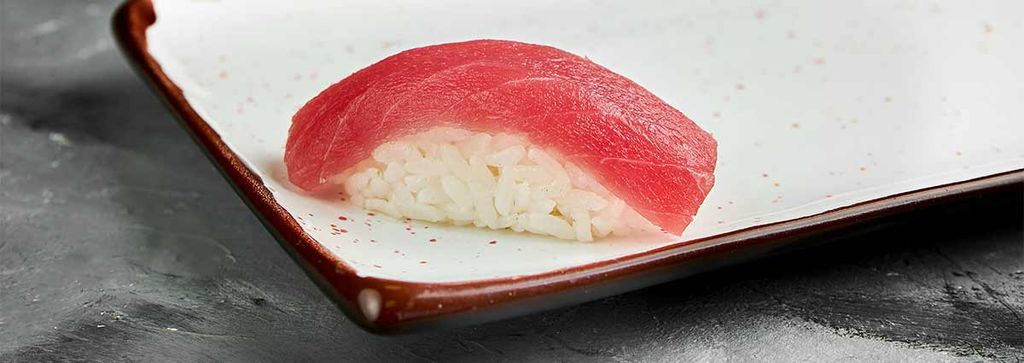 Ein Stück Nigiri-Sushi mit Thunfisch auf einem weißen Teller mit braunem Rand.