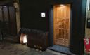 Exterior view of a small sushiya in Osaka at night, with a dark façade, wooden lattice door, and warmly lit entrance.
