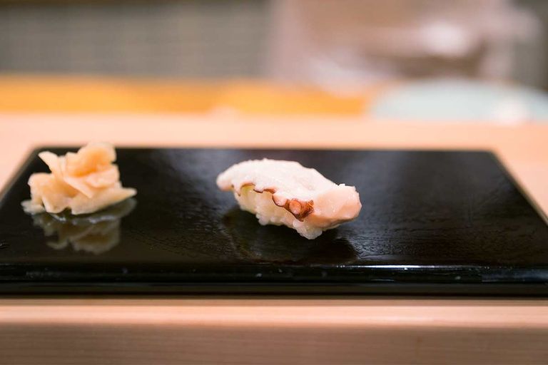 Ein Stück Tako-Sushi neben eingelegtem Ingwer auf einer schwarzen Keramikplatte