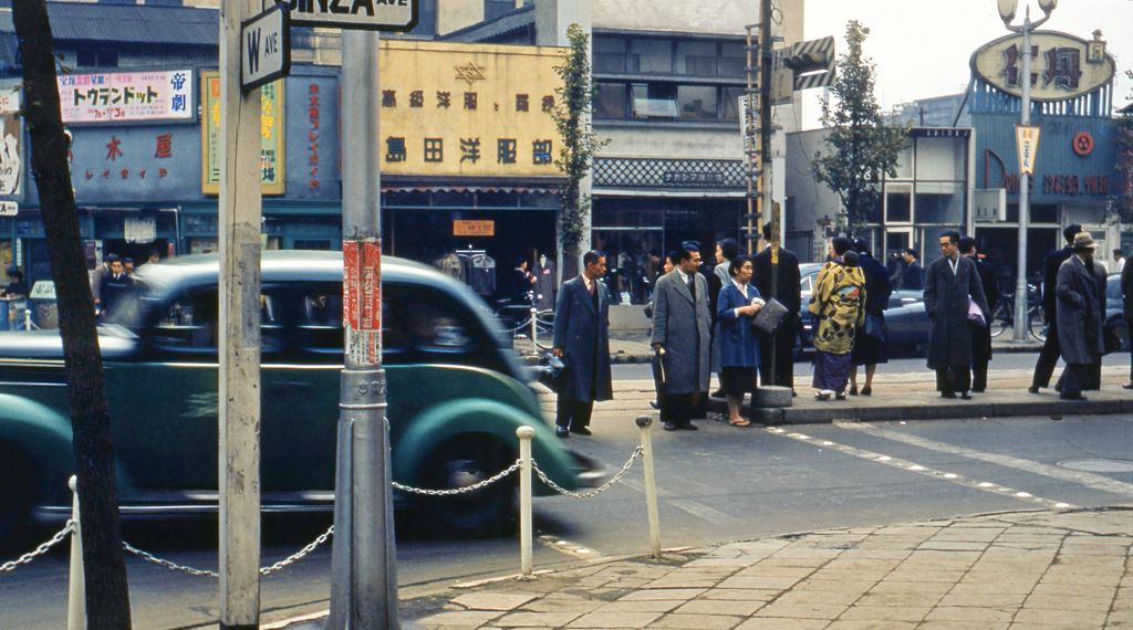 Tokio 1952, belebtes Ginza-Viertel mit Fußgängern und Oldtimern, das den wirtschaftlichen Aufschwung der Nachkriegszeit und die kulinarische Expansion illustriert.