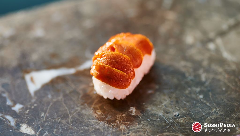 Ein Stück Uni Nigiri Sushi, bei dem Seeigel-Rogen (Uni) auf einer kleinen Portion Sushi-Reis liegt, serviert auf einer dunklen Marmoroberfläche.