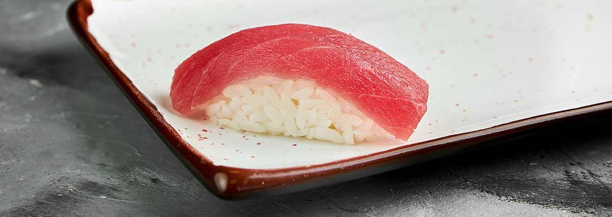 Klassisches japanisches handgeformtes Sushi mit rohem Thunfisch auf einem weißen Teller auf einem grauen Tisch.