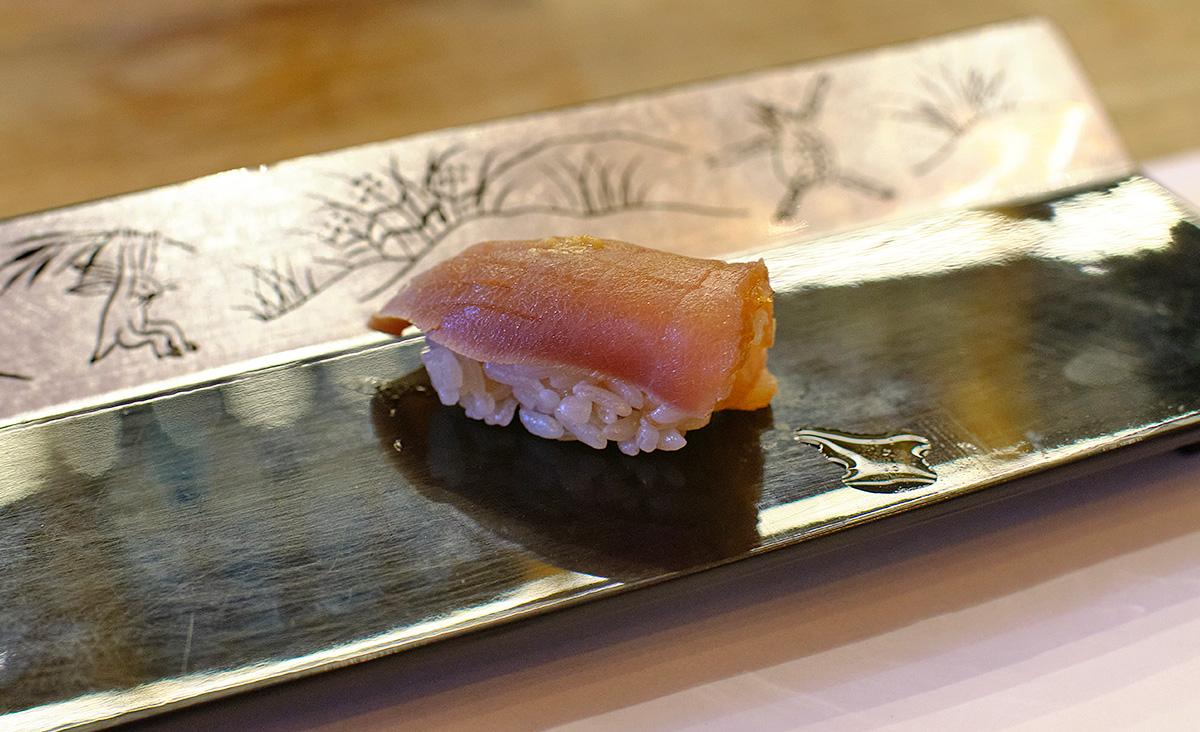 Fleisch des roten Thunfisch, das mehrere Tage gereift wurde und anschließend in Soja-Sauce eingelegt. Zubereitet als Nigiri Sushi (くらかけすし, 鞍掛寿司). 
				D. Schilder. 
				Zuke Maguro Sushi. 
				
				copyrighted ©. 
				