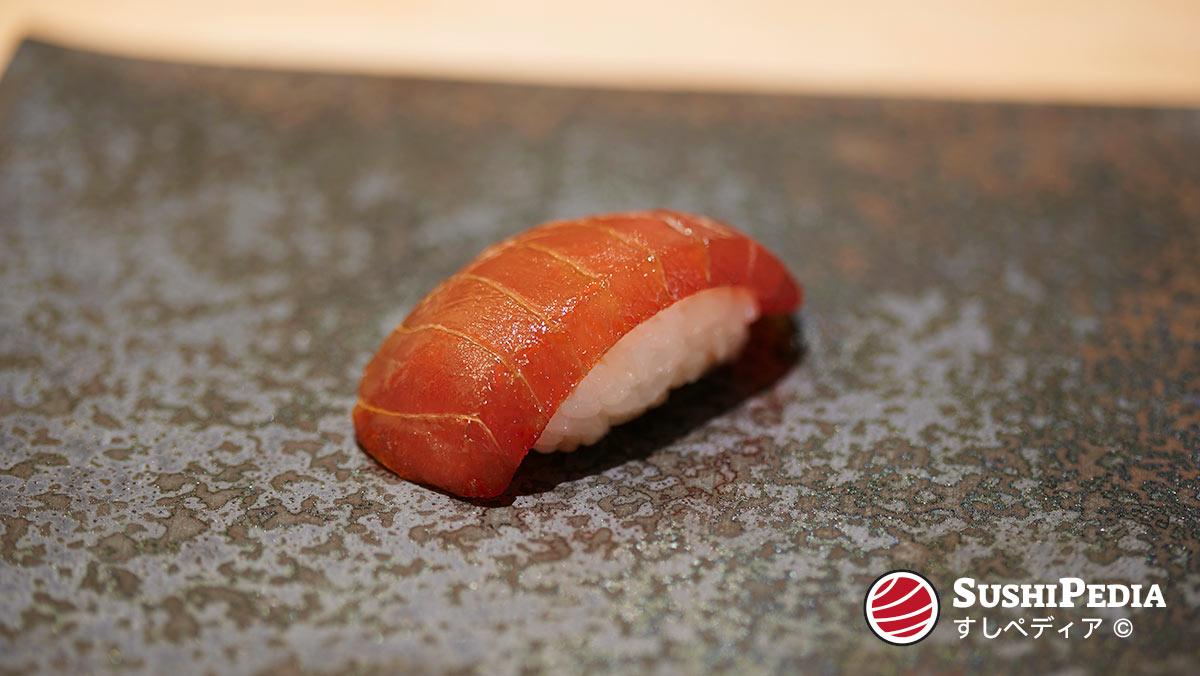 Ein Stück handgeformtes Thunfisch Maguro Nigiri Sushi liegt auf einer Tonplatte in einem Restaurant. Das Thunfisch Fleisch wurde zuvor in Soja-Sauce eingelegt und zeigt eine deutlich intensivere Farbe und samtartige Oberfläche.